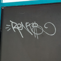 A graffiti tag of the word 'rents' written on a bus shelter in white paint.